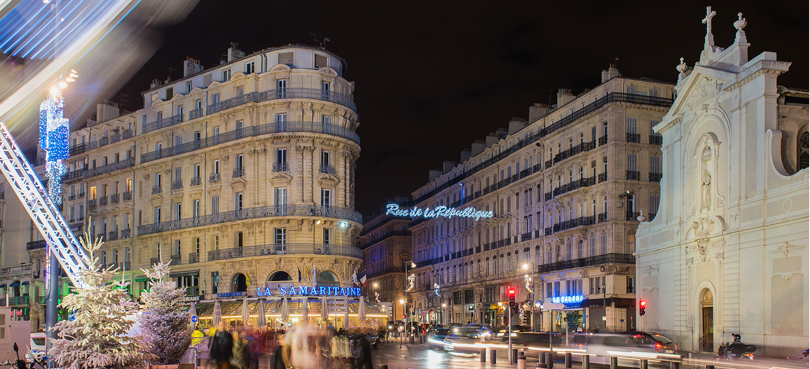 Élégante rue de ville européenne la nuit, illuminée de lumières festives, présentant une architecture classique et une atmosphère animée.
