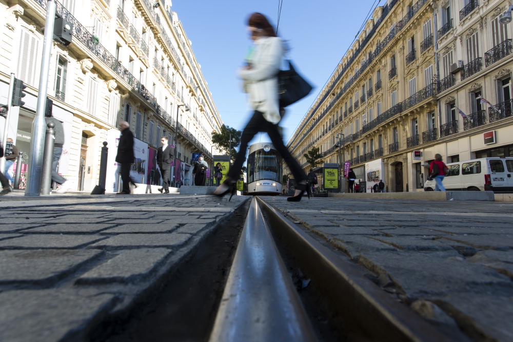 Scène urbaine moderne : un tramway sur une rue pavée bordée de grands immeubles, des piétons passant