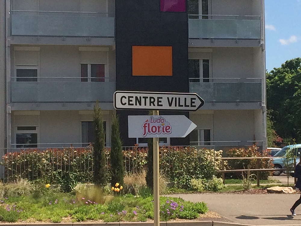 Panneau de rue indiquant la direction "Centre Ville" et "Ludo Florie", à proximité d'un immeuble résidentiel.