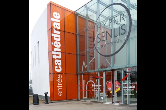 Centre commercial moderne, Hyper Senlis, comprenant 21 boutiques. Façade orange et vitrée. Entrée visible.