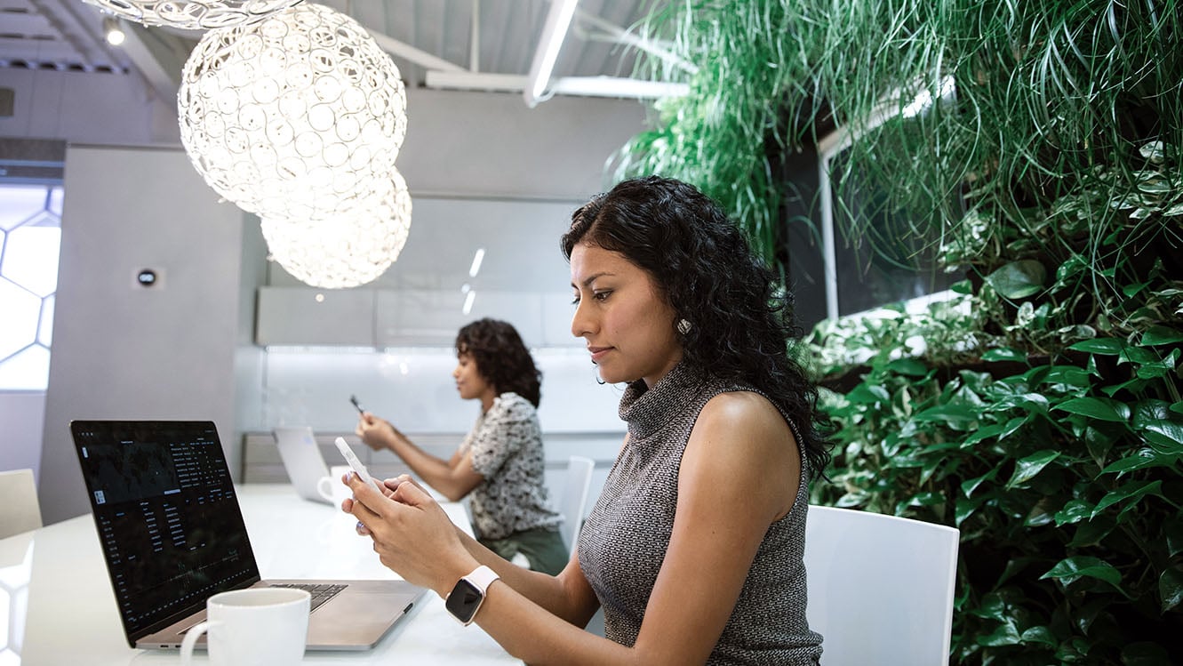 Two people sitting at a desk looking at their phones