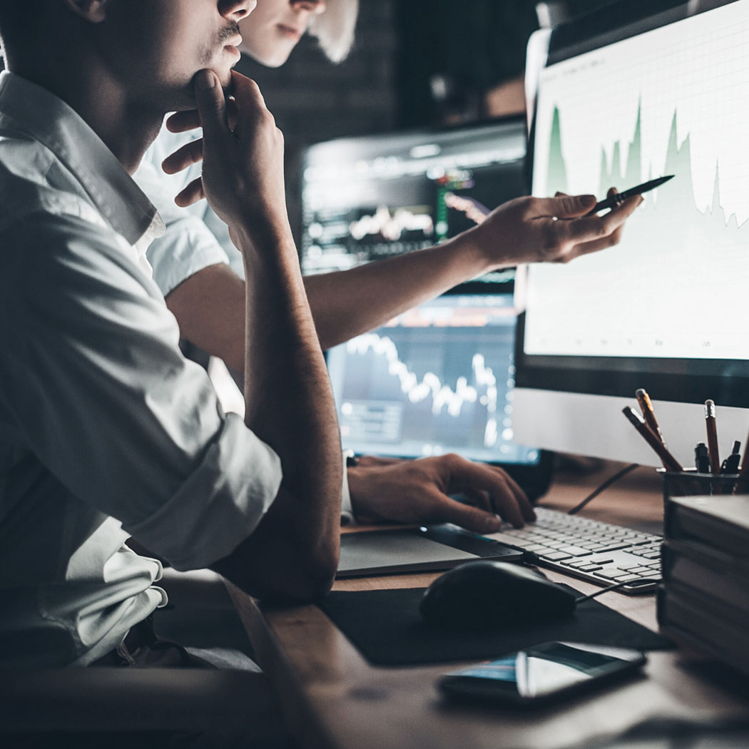  Team analyzing digital market trend charts on multiple computer screens in an office setting.