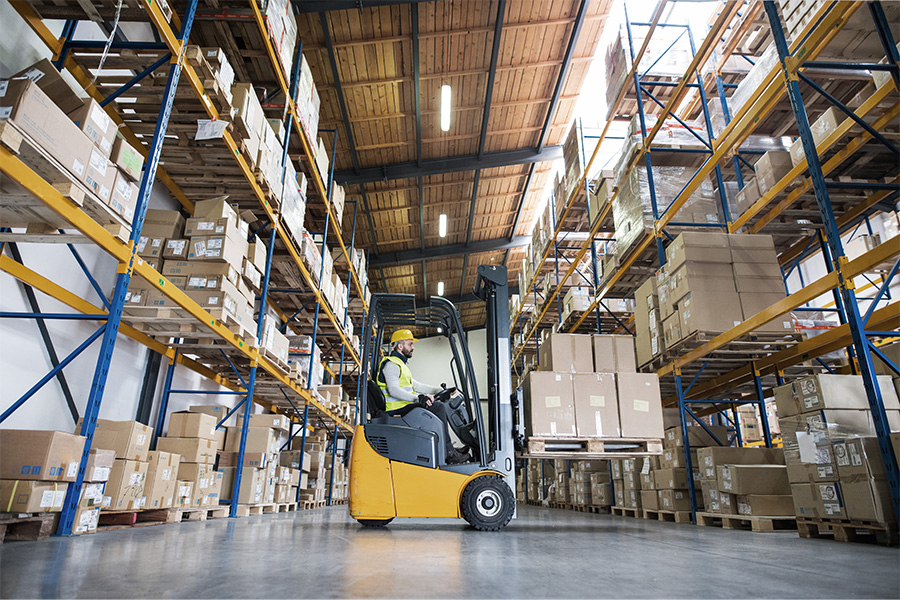Worker operating a forklift in a warehouse with tall shelves.