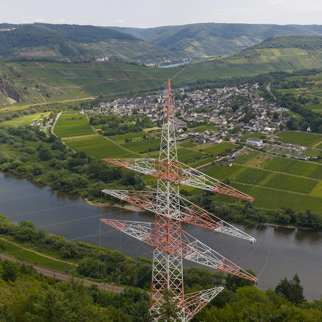 High-voltage transmission tower overlooking a river valley and rural village with green hills in the background