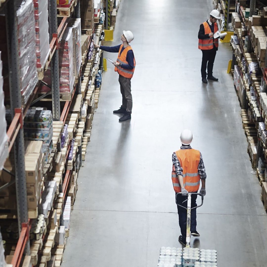 Three warehouse workers in safety vests managing inventory on shelves