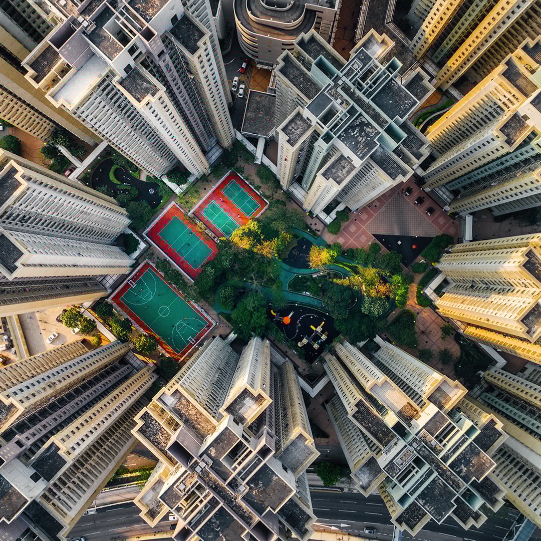 Aerial view of tall residential buildings surrounding sports courts and green park area in an urban cityscape