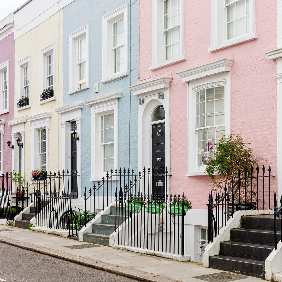 Row of pastel-colored townhouses with black railings and red, pink, and blue doors on a quiet street