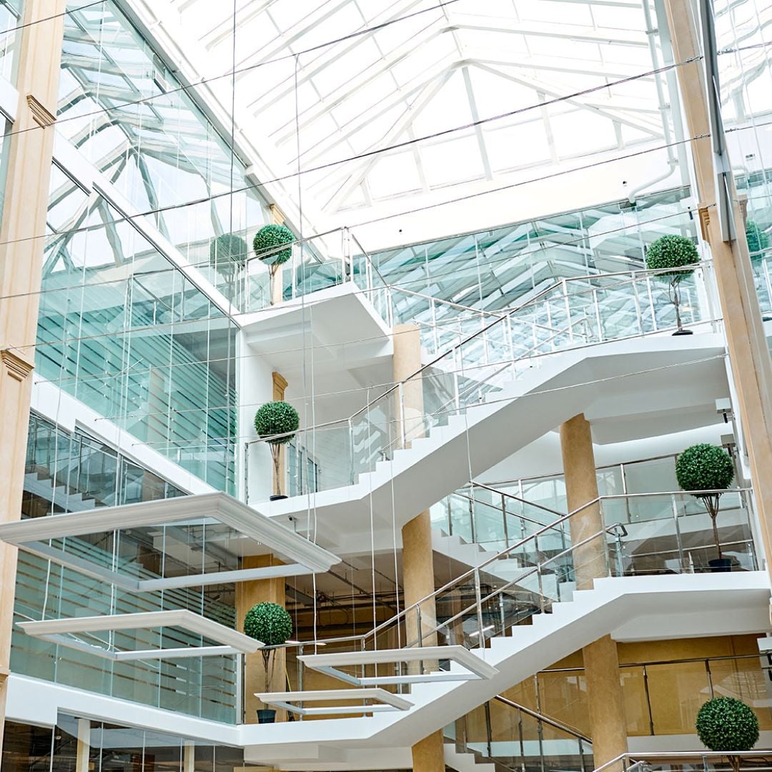 Modern glass atrium with white staircases and potted green plants.