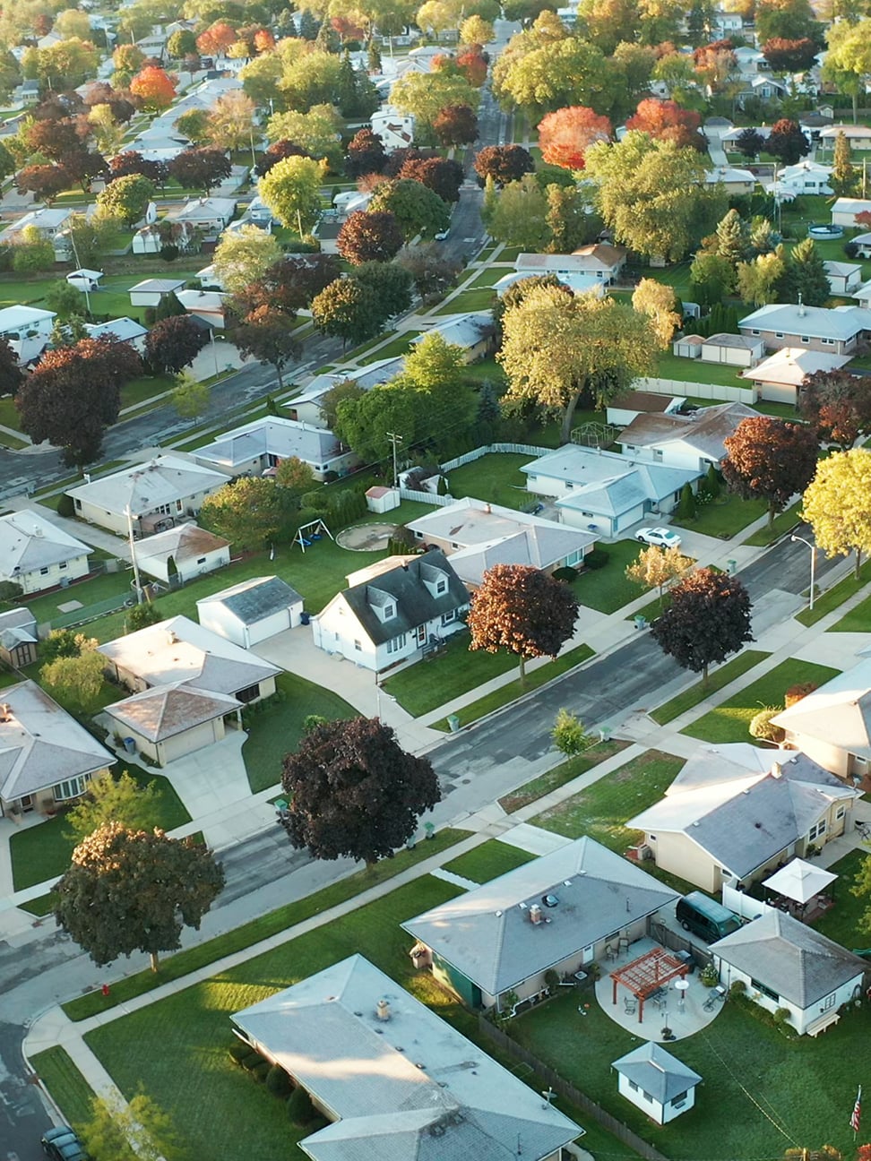Aerial view of a suburban neighborhood with single-family homes, tree-lined streets, and green lawns.