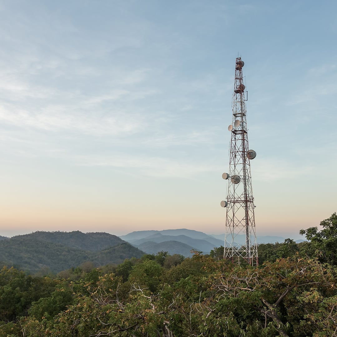 Telecommunications tower on a forested mountain ridge with rolling hills in the background at sunset