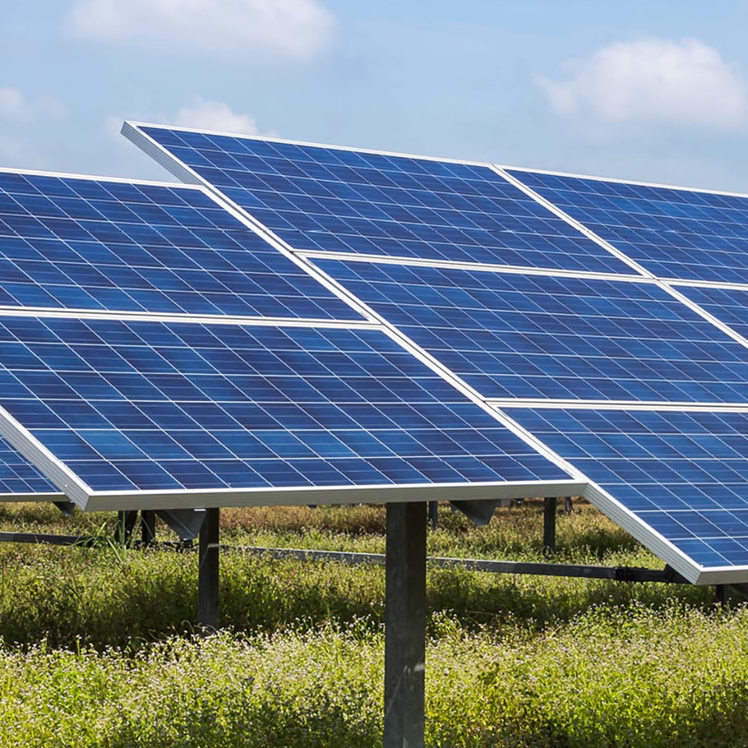 Rows of utility-scale solar photovoltaic panels on ground-mounted trackers in a green field under a partly cloudy blue sky