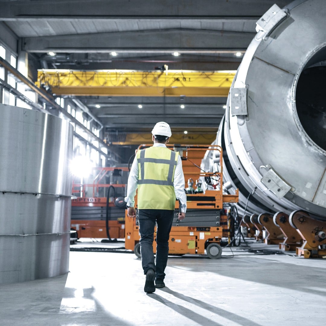 Worker in hard hat and safety vest walking through an industrial manufacturing facility