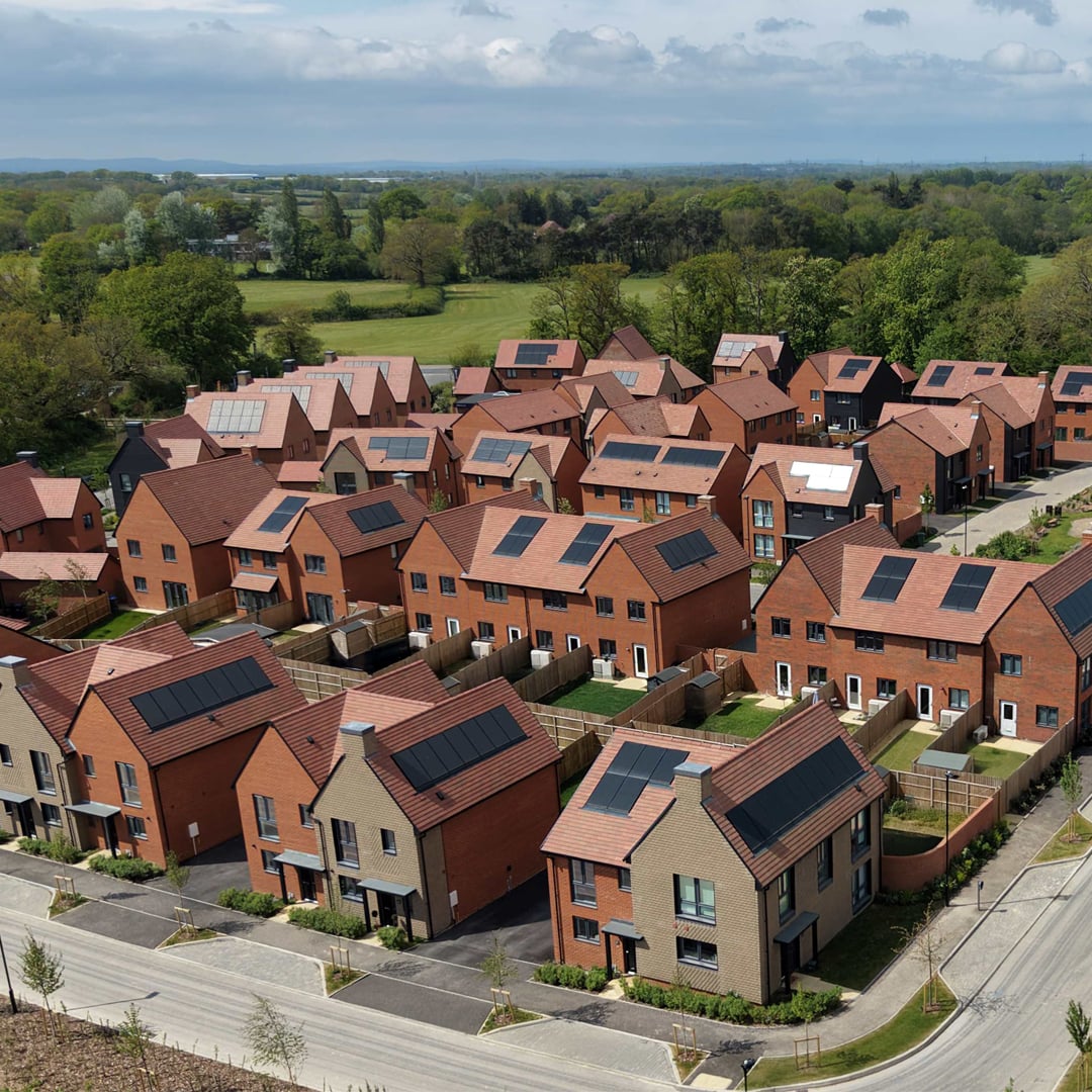 Aerial view of new single-family homes with solar panels, fenced backyards, and suburban neighborhood layout surrounded by green space