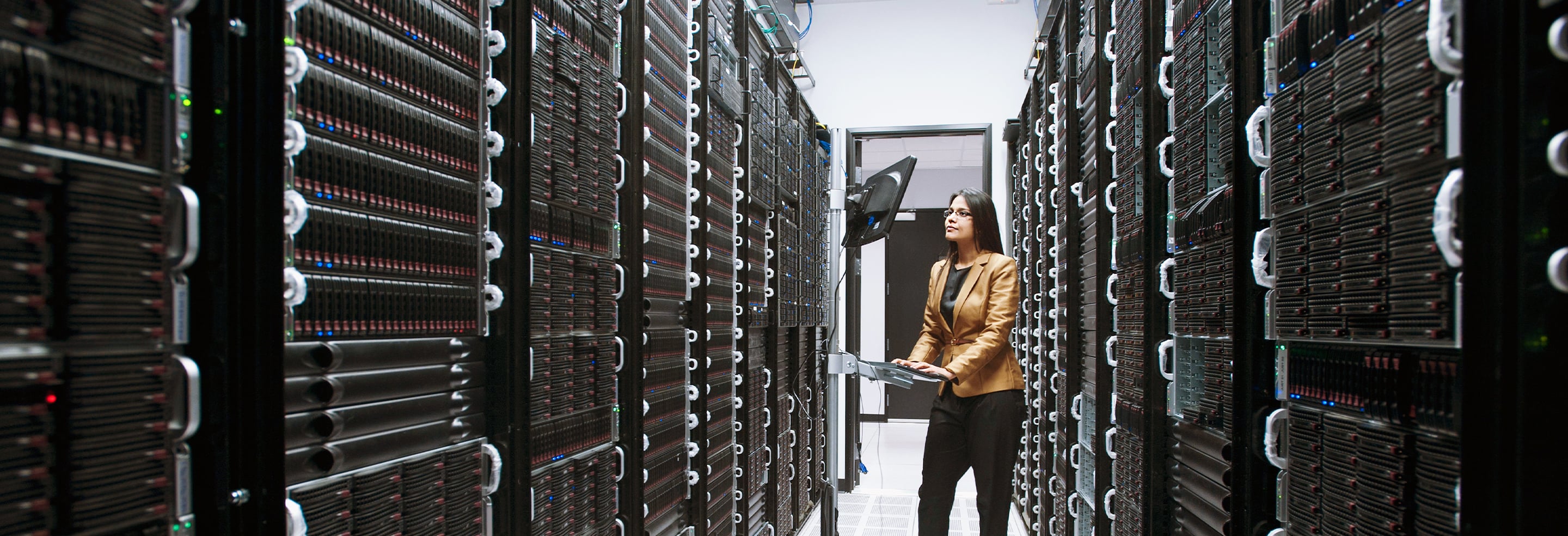 Aisle of data center server racks with active equipment and a laptop workstation