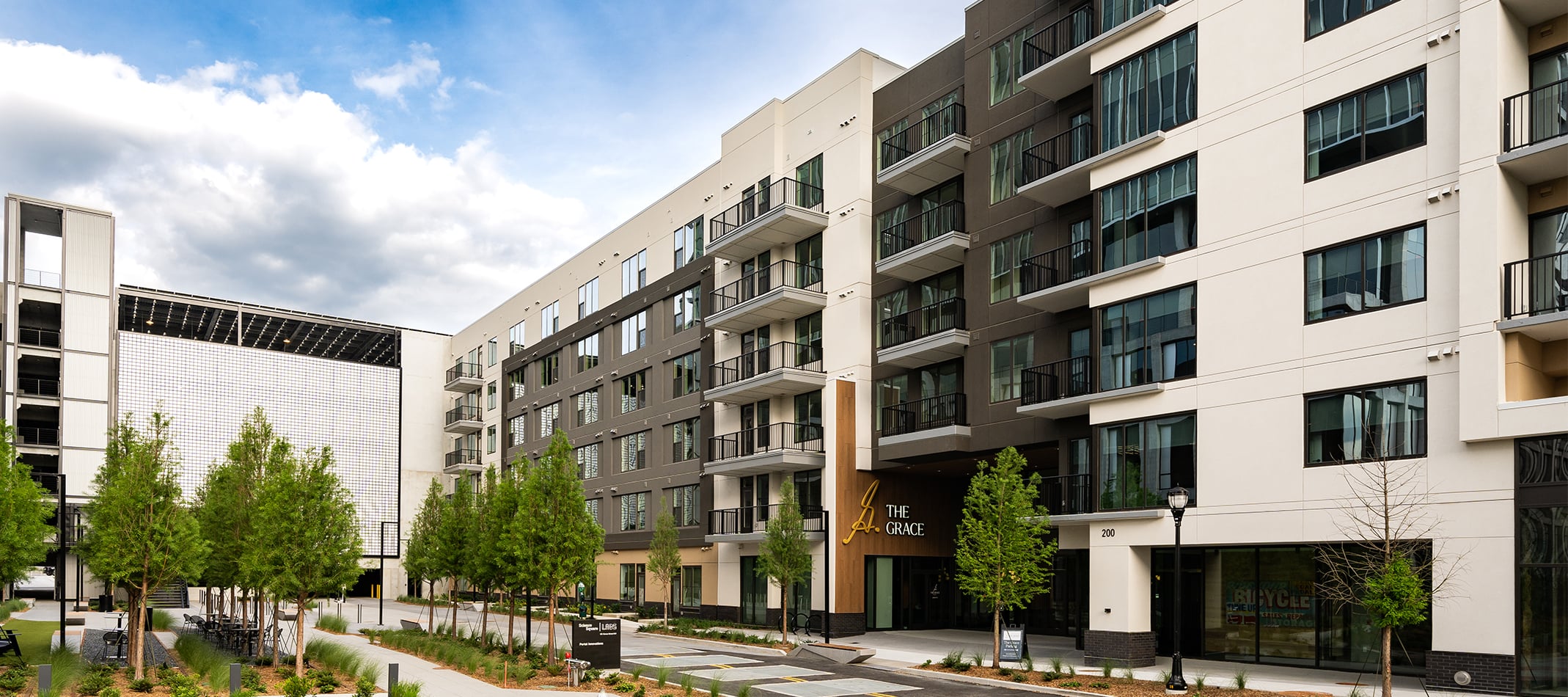 Exterior view of The Grace apartment building with balconies and landscaped walkway under a partly cloudy sky