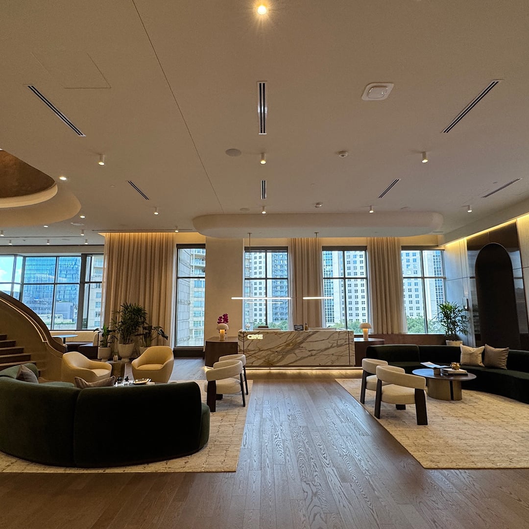 Spacious modern office lobby featuring marble reception desk, elegant seating area, large windows with city view, and contemporary lighting