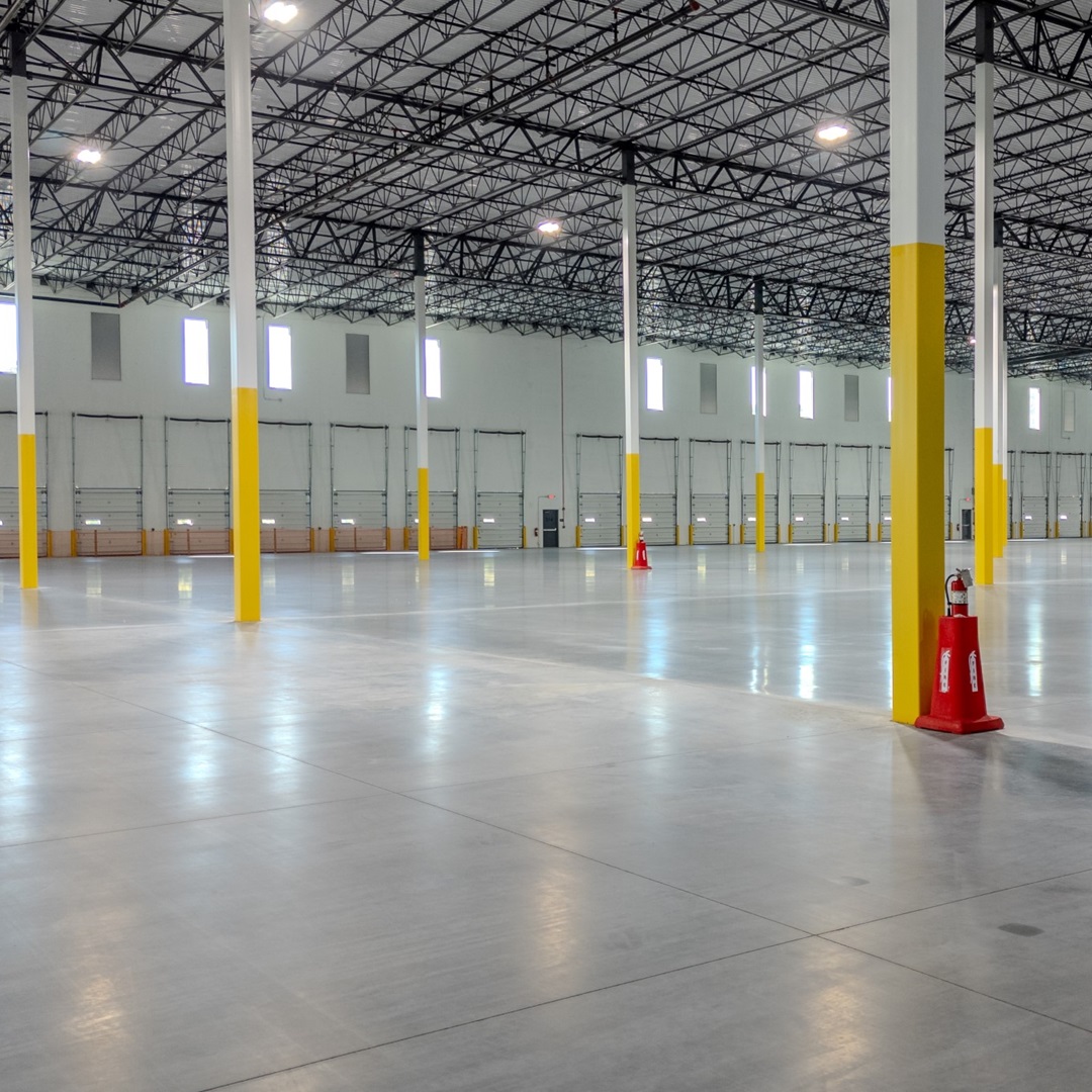 Interior of a modern industrial warehouse with high ceilings, concrete floors, dock doors, and structural columns suited for logistics or distribution use.