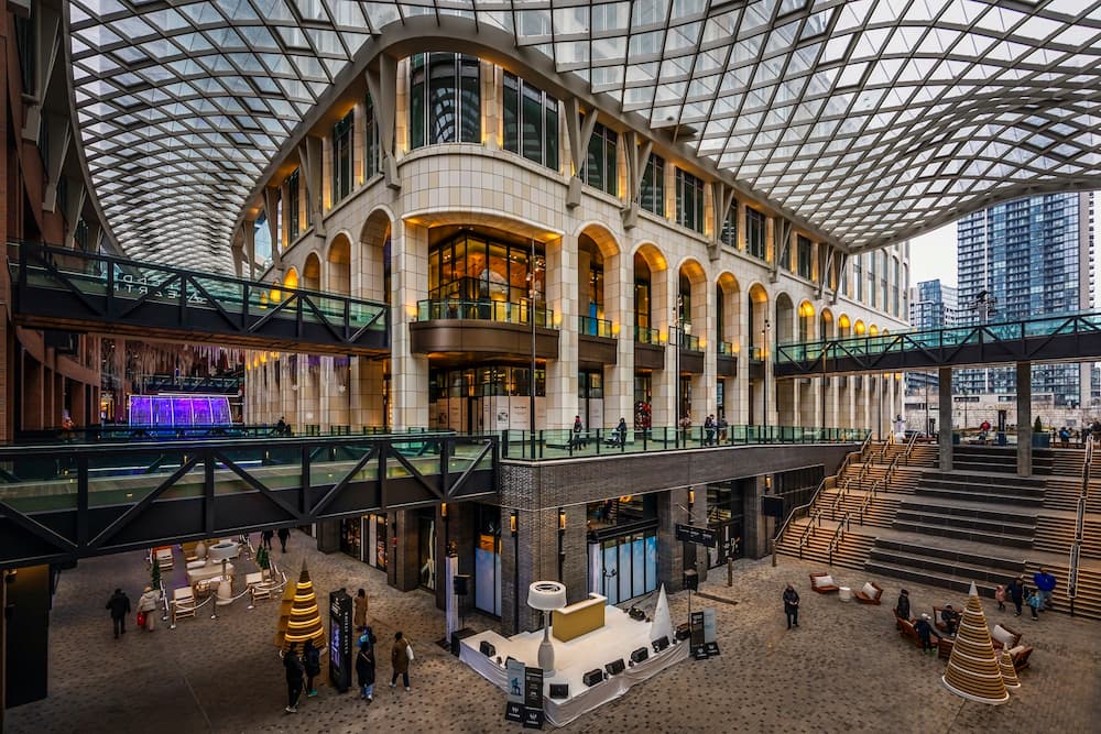 The Well - Covered courtyard with a glass lattice roof, arched facades, and people walking below