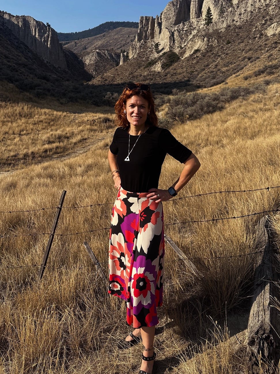 Rebecca Godfrey standing in front of Kamloops tall rock formations and hills in the background under a clear blue sky.