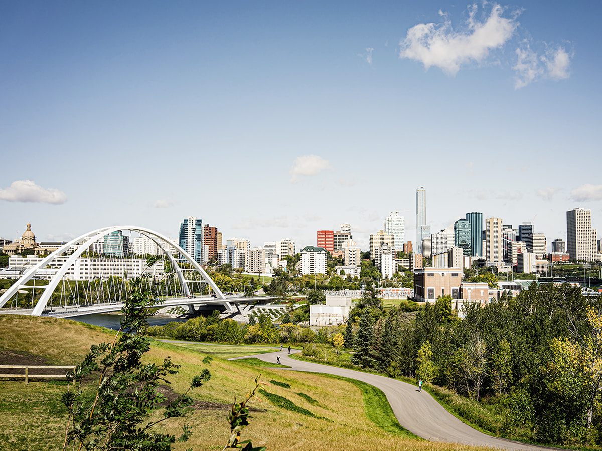 Panoramic view of Edmonton skyline featuring the Walterdale Bridge, lush greenery, and a clear blue sky, showcasing the city’s blend of urban architecture and natural landscapes