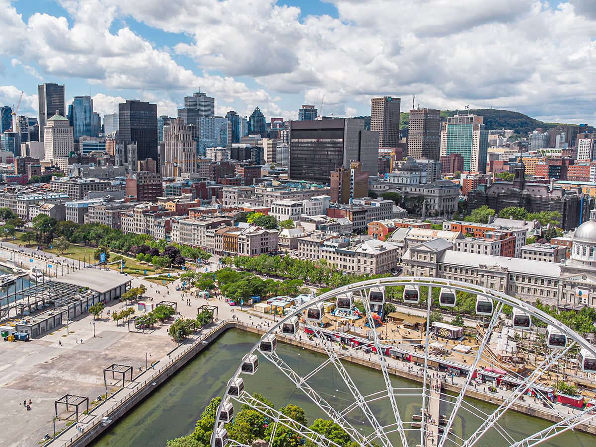 Aerial view of downtown Saint-Laurent showcasing the vibrant cityscape with diverse architecture, green spaces, and the iconic Ferris wheel near the waterfront, under a partly cloudy sky – highlighting the dynamic urban environment