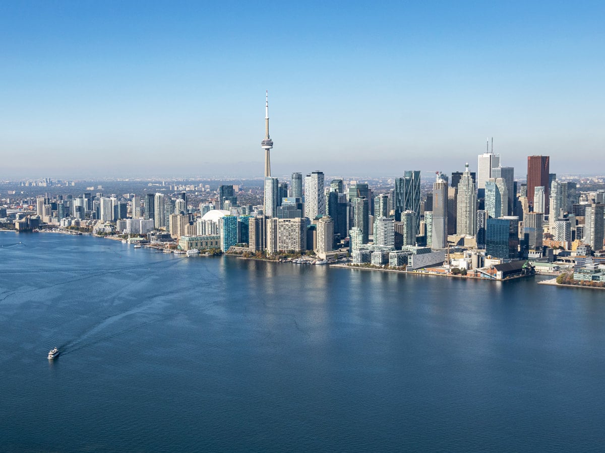 A panoramic view of Toronto’s downtown skyline featuring the iconic CN Tower, modern skyscrapers, and Lake Ontario with a boat sailing on the water, representing the bustling urban life and economic vitality of Canada’s largest city