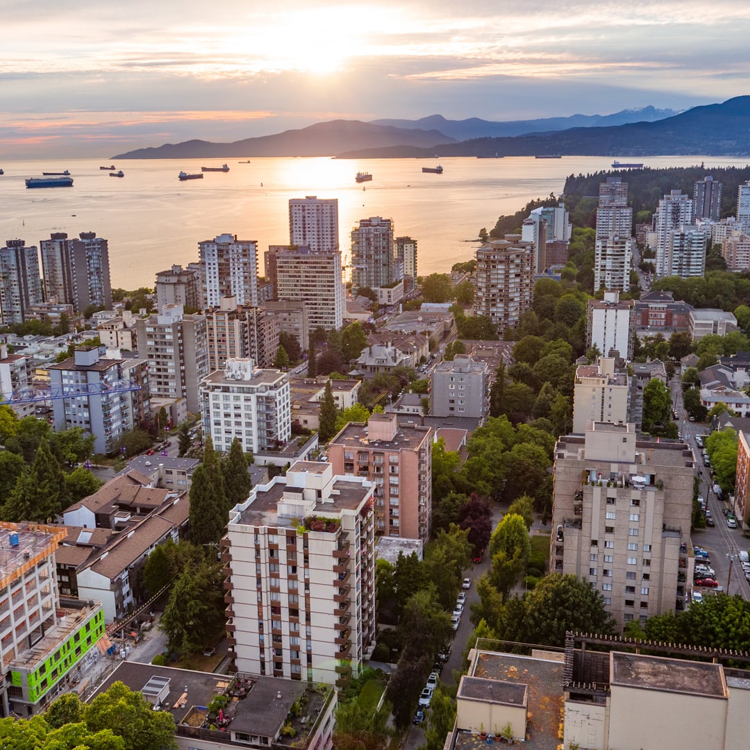 Aerial view of multifamily apartment buildings in Vancouver at sunset, overlooking the water and distant mountains.