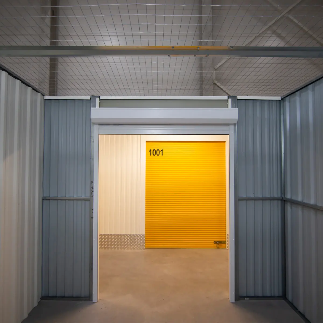 A view from within a self-storage unit hallway showing a bright yellow corrugated roller door with the number "1001" on it.