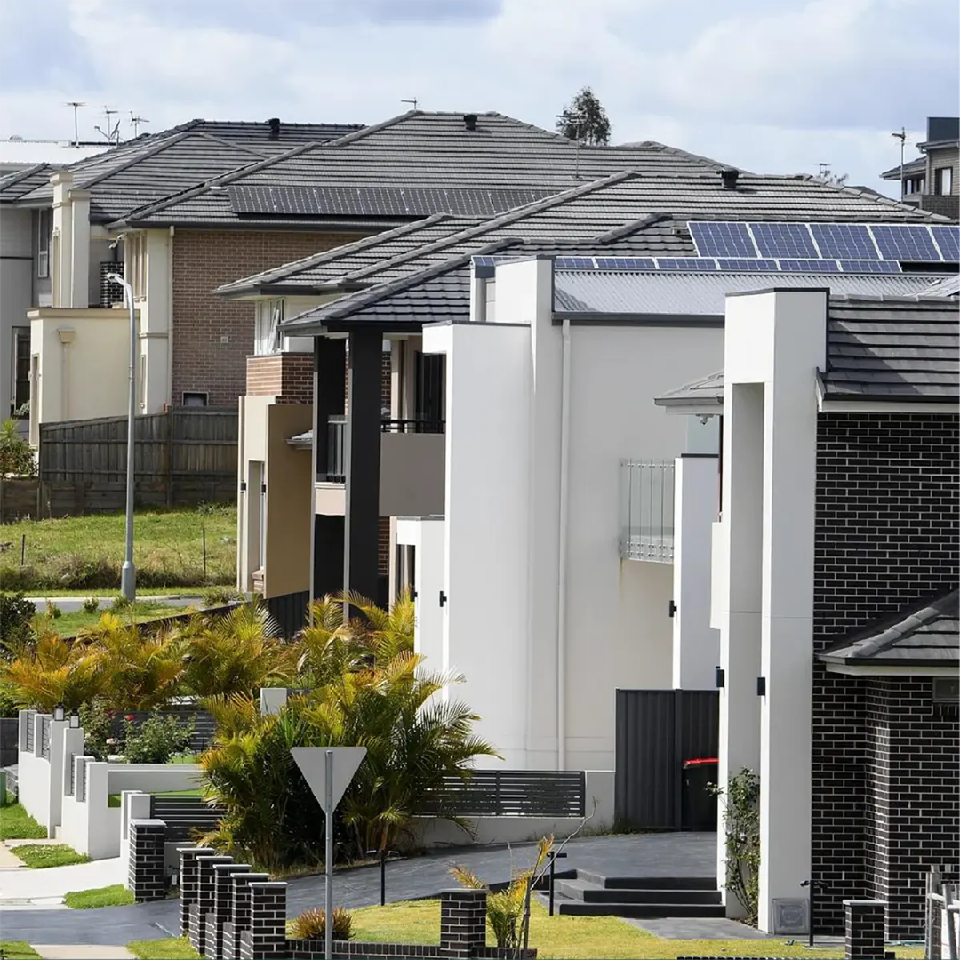 A row of modern suburban houses in Australia, featuring tiled roofs with solar panels, brick and rendered facades, and neat front gardens.