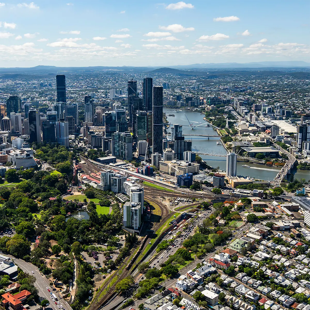 An aerial view of the Brisbane CBD featuring the winding Brisbane River, the dense cluster of skyscrapers, and Roma Street Parkland in the foreground.