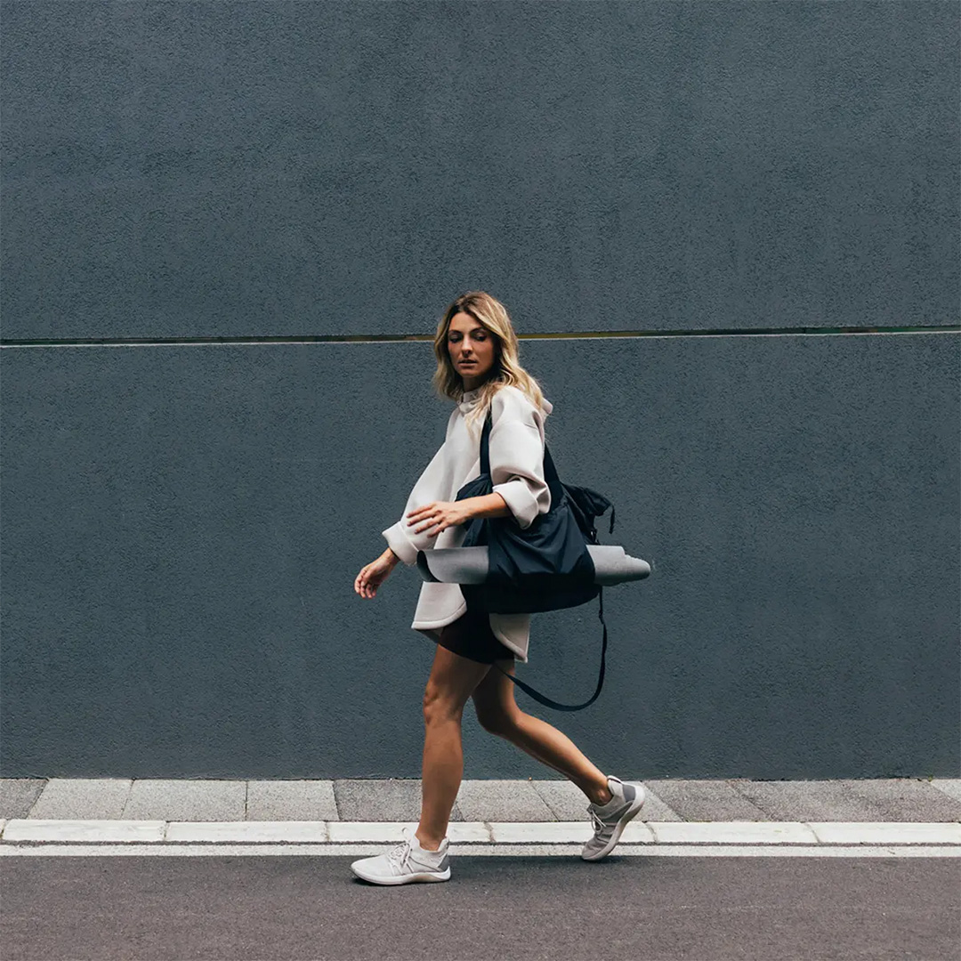 Woman walking down the street carrying a yoga mat.