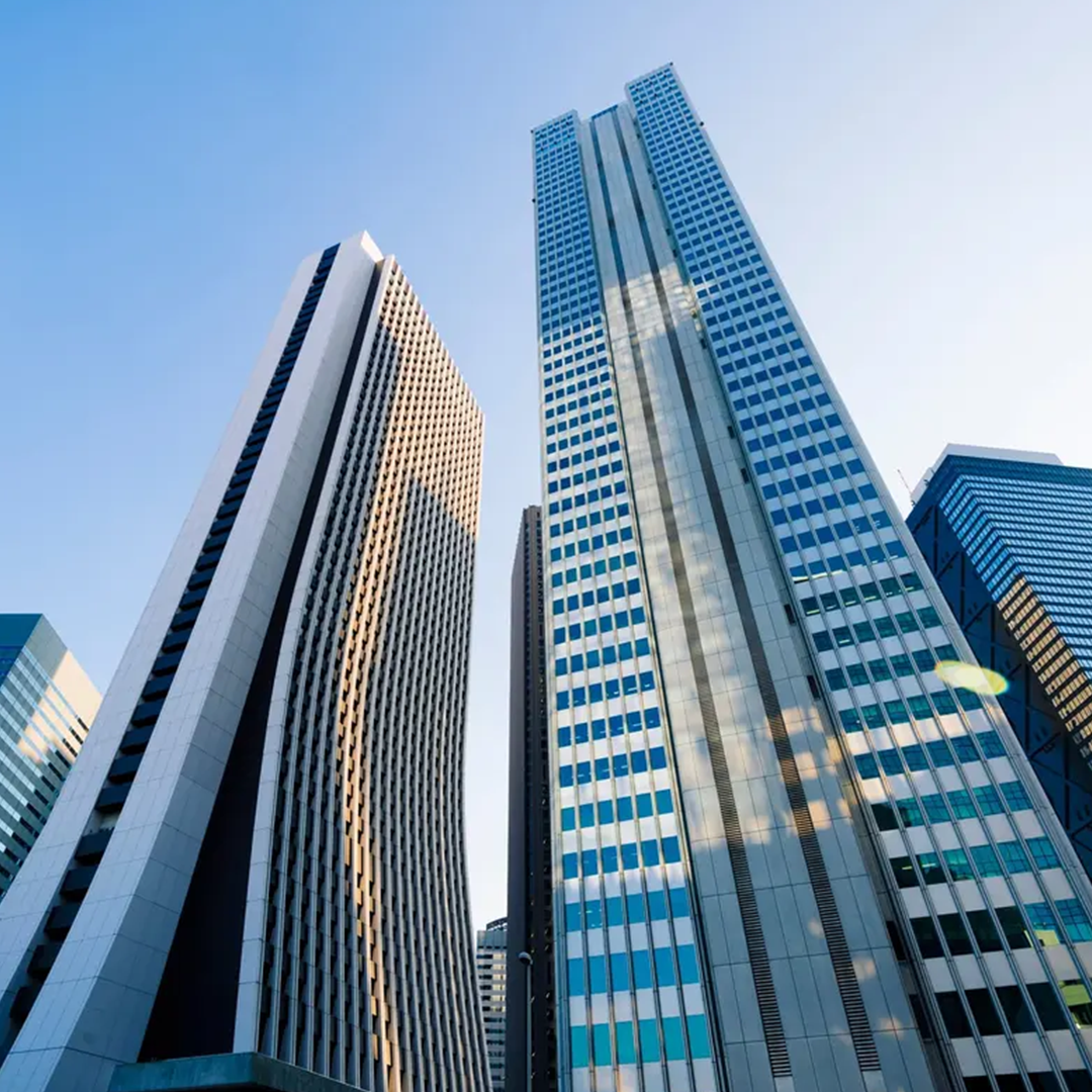 Looking up at multiple towering skyscrapers with modern glass facades and geometric patterns under a clear blue sky.