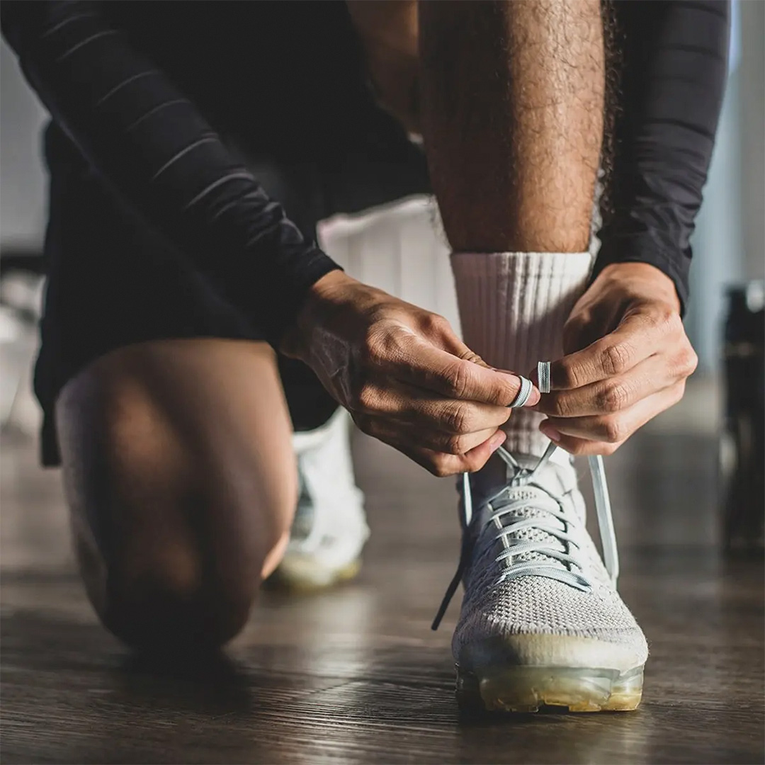 Close-up of a person kneeling to tie their trainers.