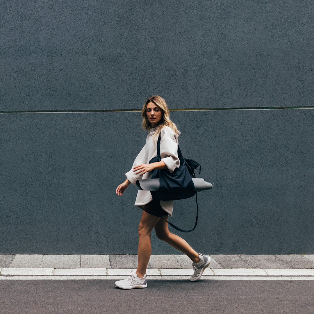 A woman walks down the street, carrying a yoga mat and bag.