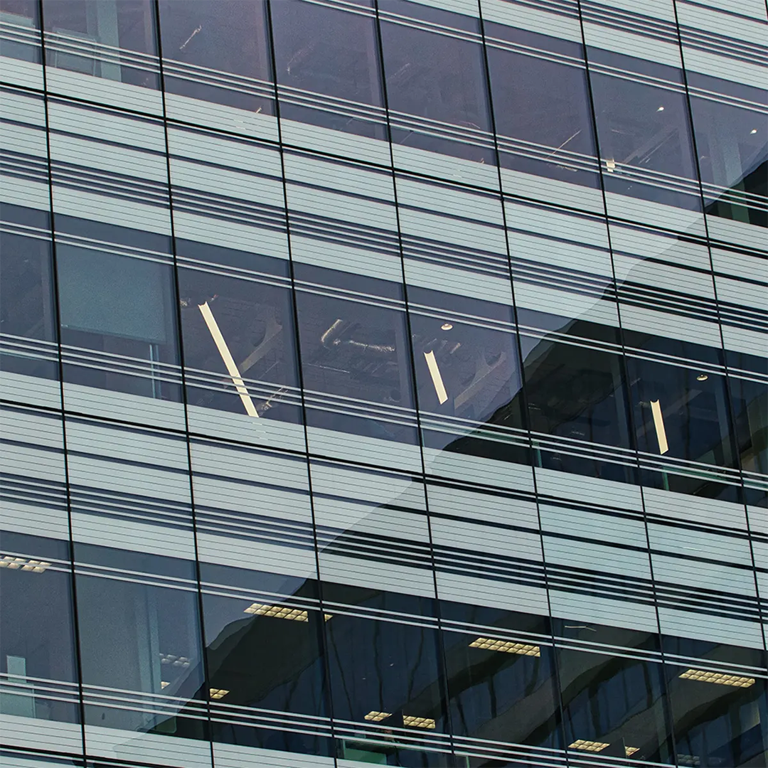 A close-up view of a modern glass skyscraper shows its windows reflecting light and revealing office interiors.