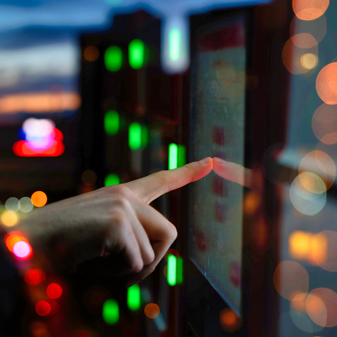 A person's finger touches a glowing interactive screen against a blurred background of city lights at night.