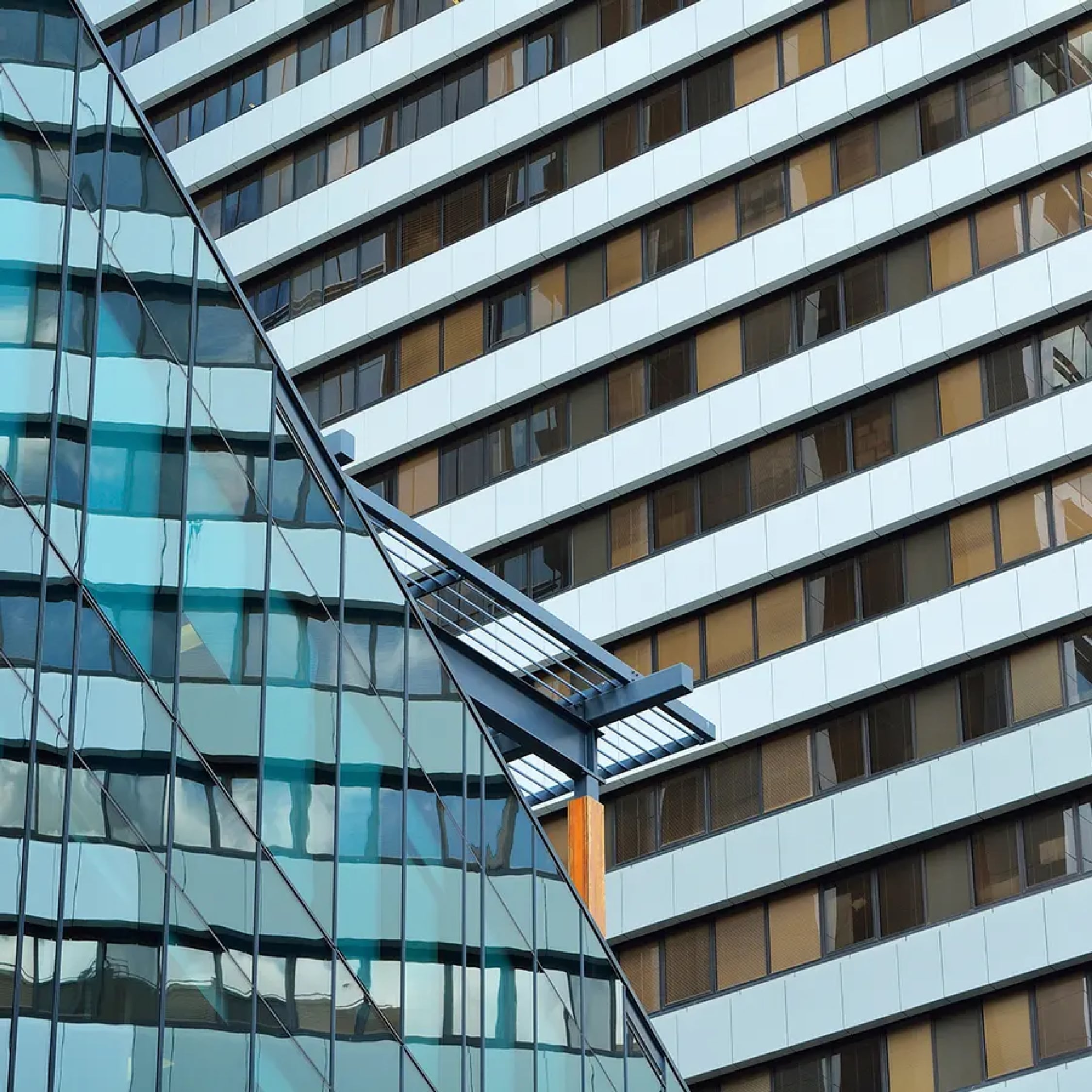 A sharp, angular glass facade overlaps the side of a tall building featuring a pattern of white horizontal bands and darkened, recessed windows.