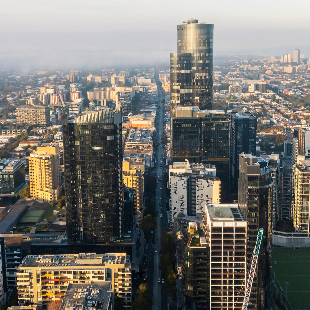 An aerial view of a bustling Melbourne city street lined with modern high-rise apartments and skyscrapers bathed in the warm, golden light of early morning.