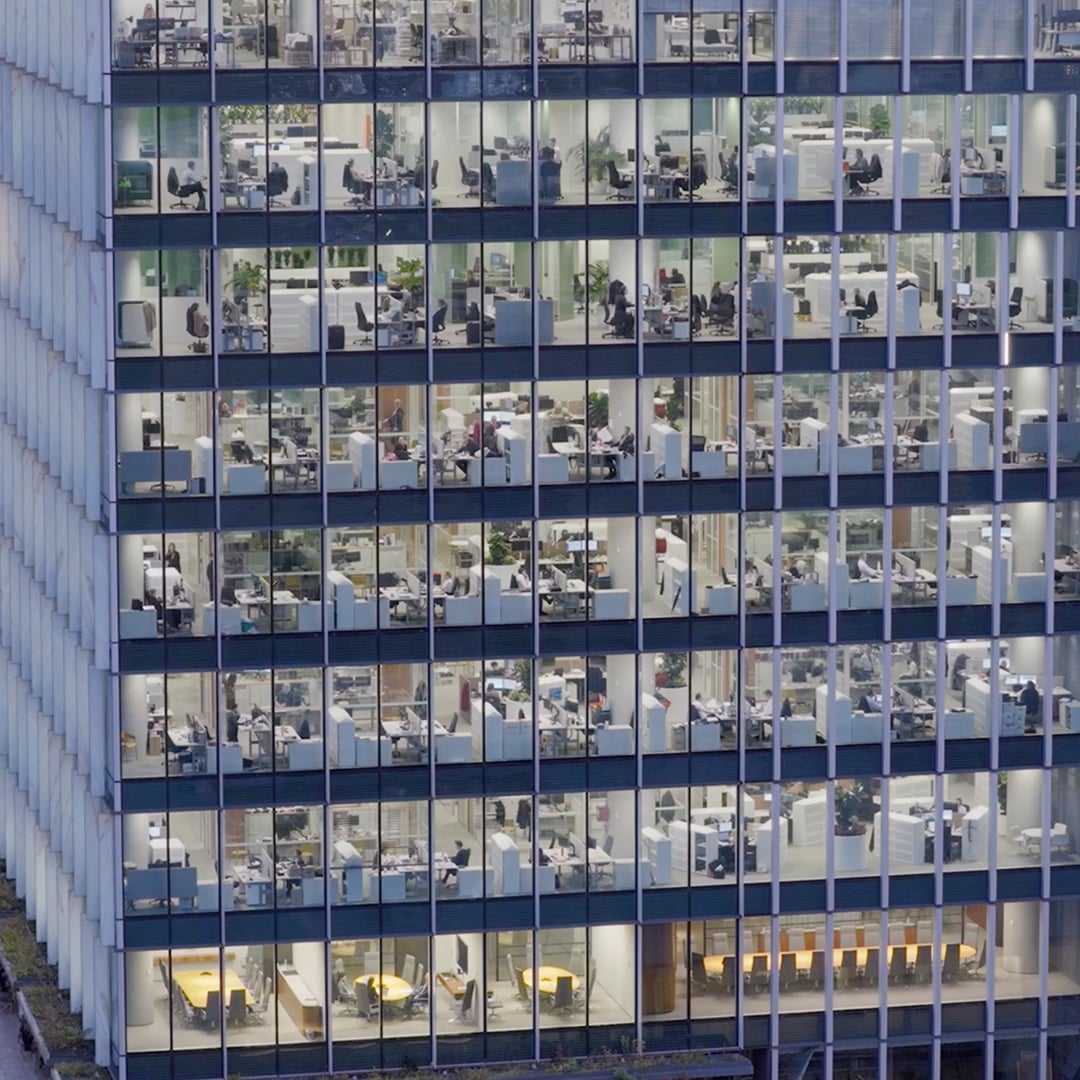 High-angle view of a modern office building with illuminated floors, desks, cubicles, and employees working late.