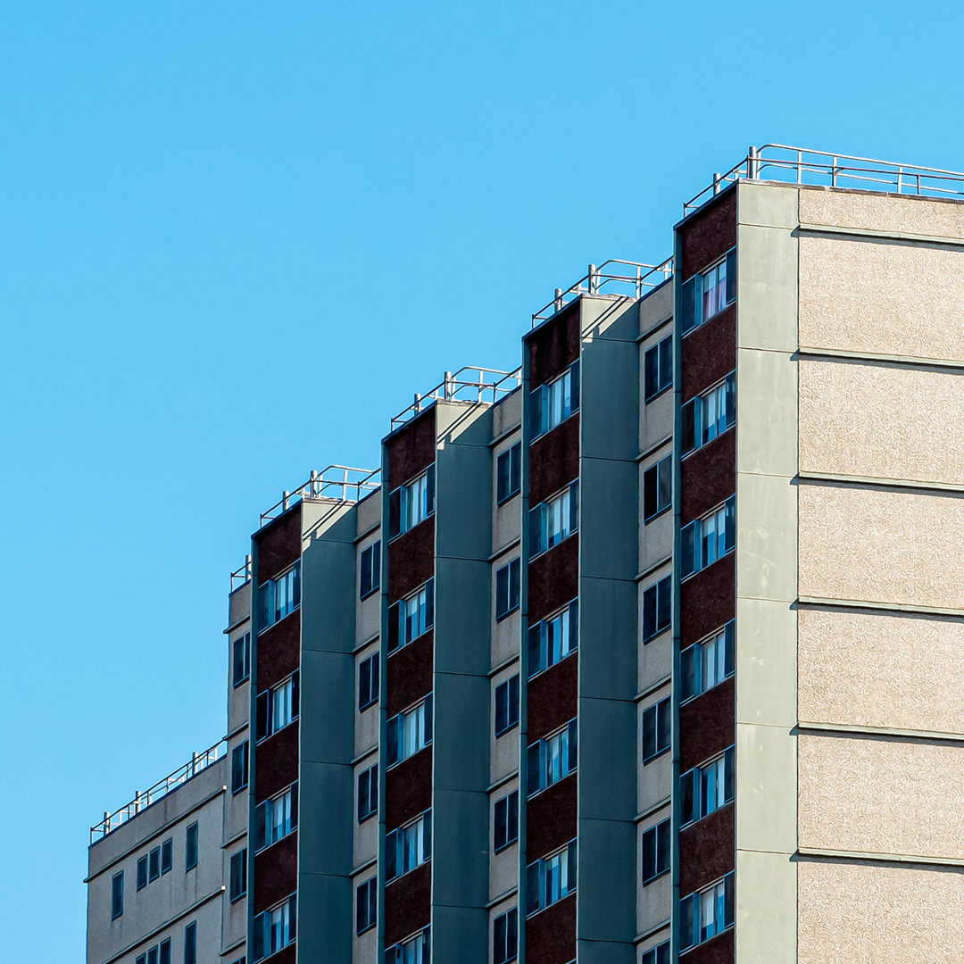 A building under construction, covered in a network of wooden and metal scaffolding, reaches towards a clear blue sky.