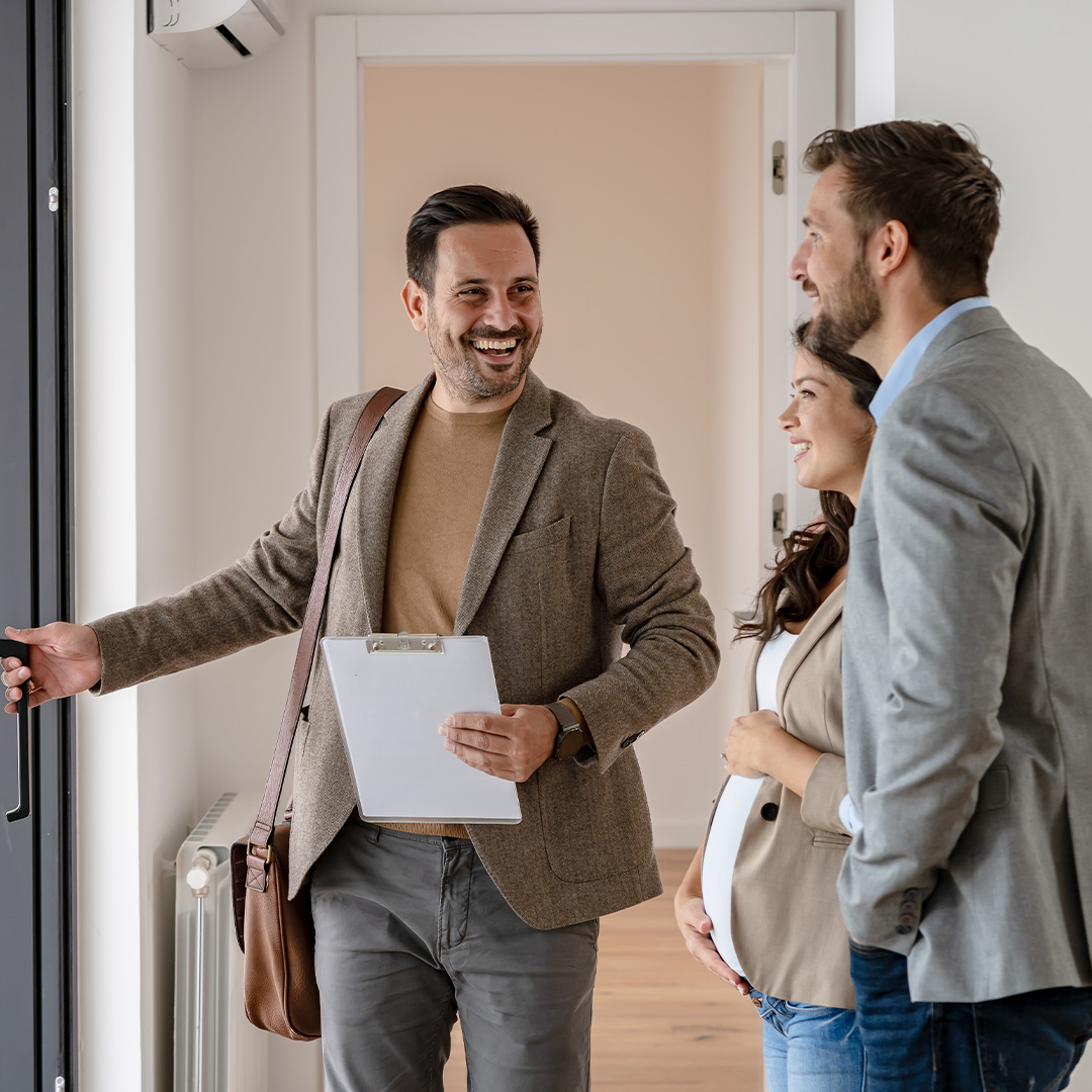 The image shows a real estate agent showing a couple a newly built apartment that they are interested in purchasing.