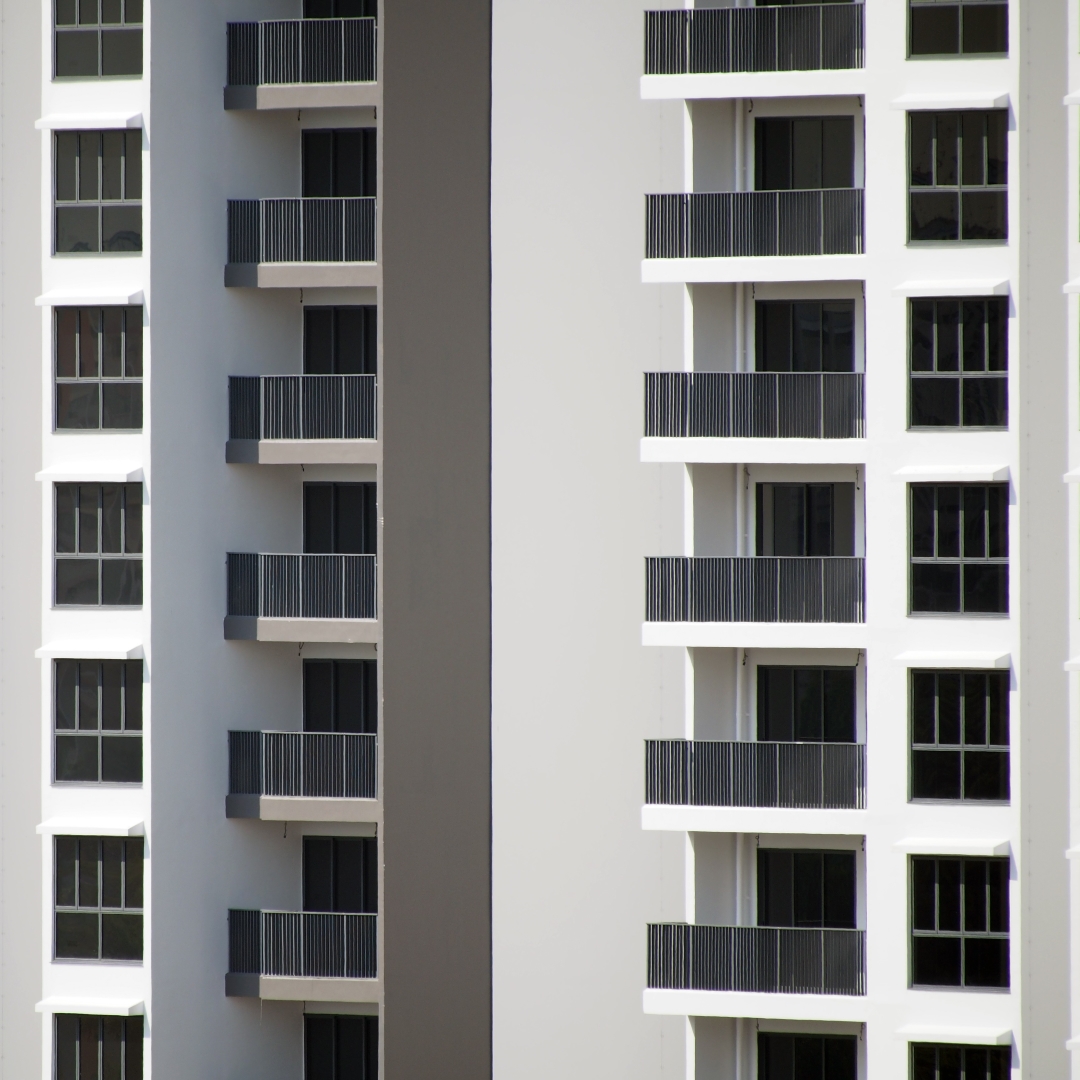 A close-up view of two modern high-rise buildings with repeating patterns of windows and balconies, one on the left with grey walls and the other on the right with white walls