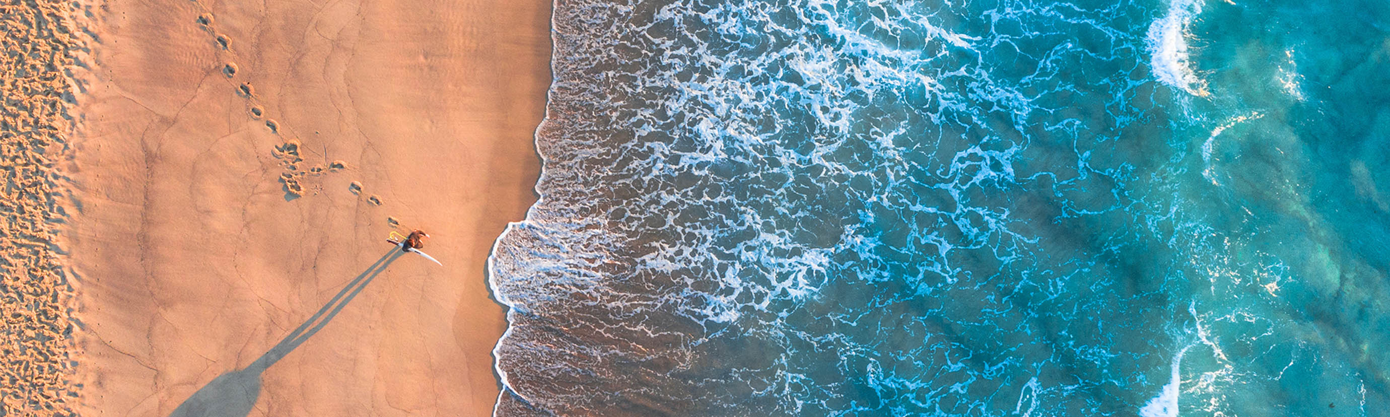 Aerial view of a person walking along a beach, representing CBRE’s strategic property consulting journey from sustainability and infrastructure to workplace and transaction solutions. 