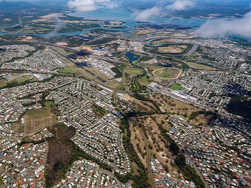 Aerial view of a suburban landscape with residential areas, industrial zones, green spaces, and a coastal waterway, highlighting urban planning and development opportunities. 