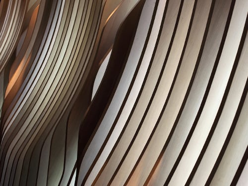 Curved vertical wooden slats in natural tones, symbolising seamless and integrated consulting solutions across all dimensions of property. 