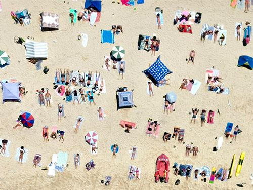 Aerial view of a crowded beach with people sunbathing, relaxing under umbrellas, and enjoying summer activities on the sand. 