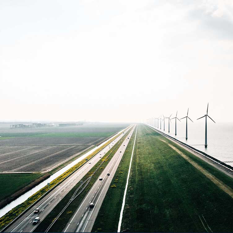 Aerial photo of a road along a dyke with wind turbines on the water side, illustrating sustainable energy and ESG-driven infrastructure.