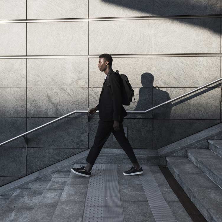 A person in business attire walks down a staircase in an urban setting.