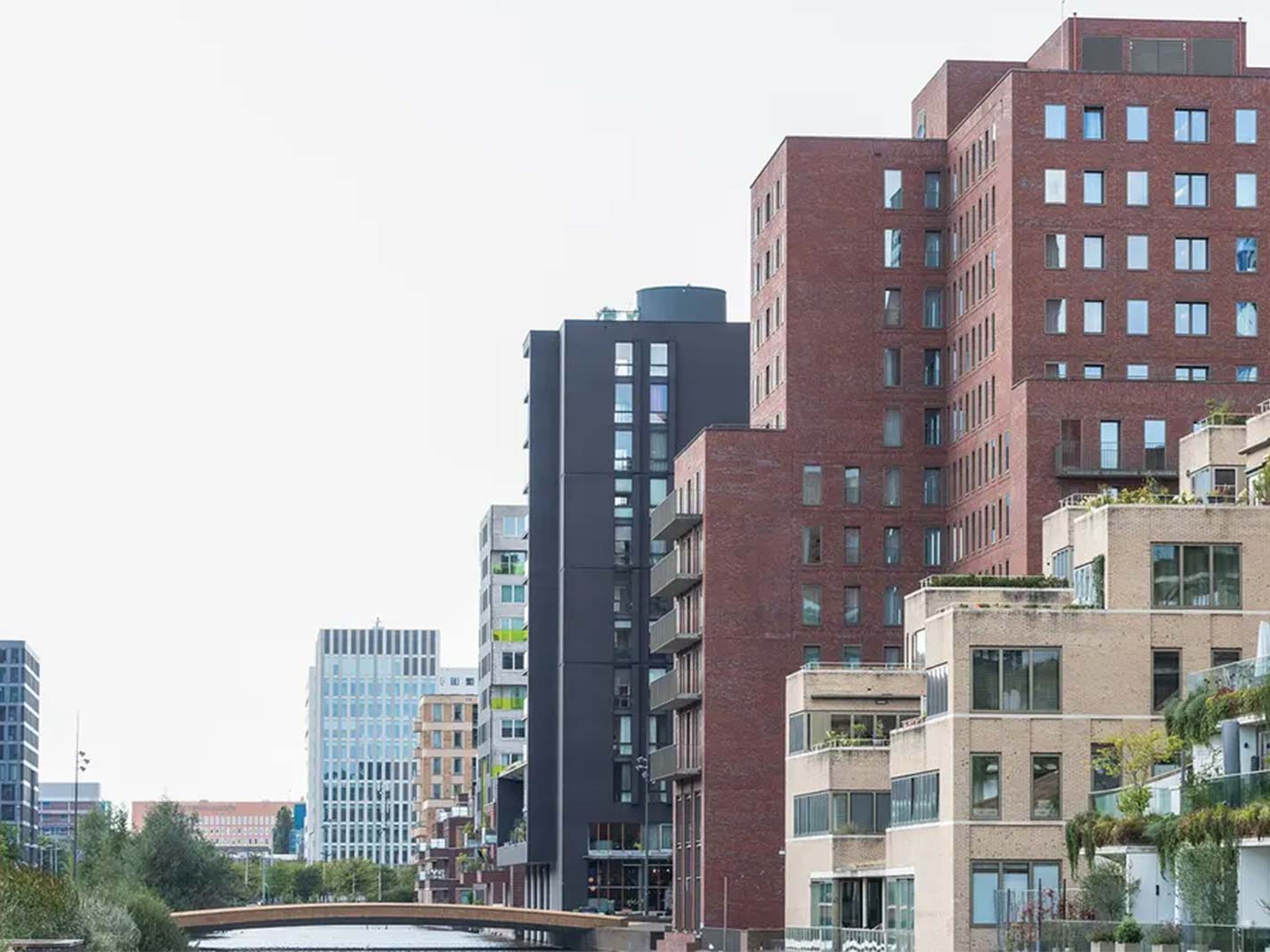 Moderne stedelijke skyline in Amsterdam met hoogbouw in diverse architectonische stijlen langs een kanaal met brug.
