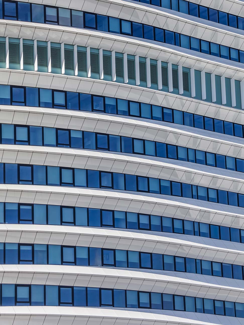 Gevel van hoog kantoorgebouw met blauw glazen ramen en witte gevelpanelen in strak patroon, geschikt voor zakelijke vastgoed, kantoren en architectuur.